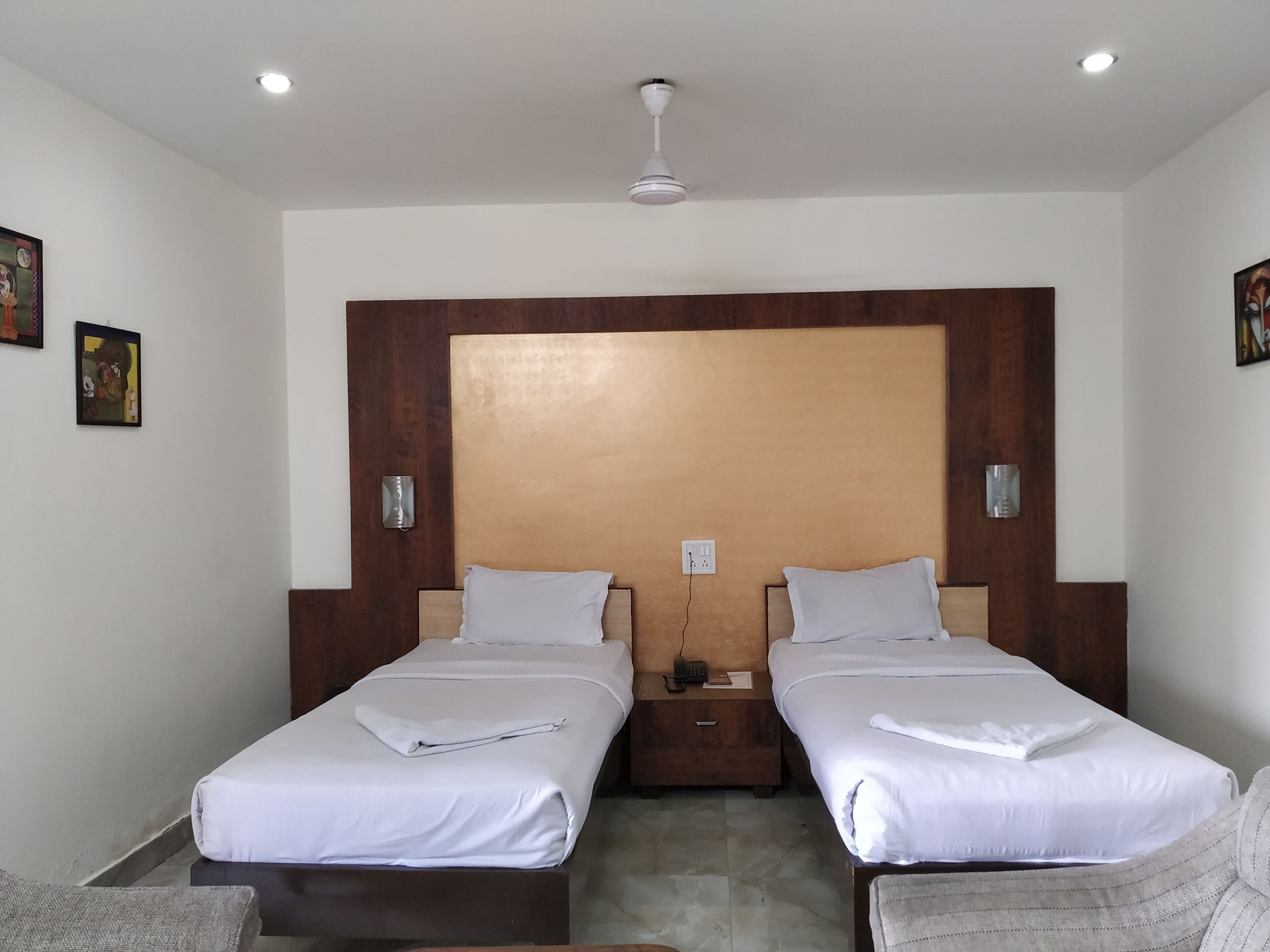 Ein Hotelzimmer mit zwei Einzelbetten, einem hölzernen Kopfteil, einem Nachttisch mit Telefon und einem Deckenventilator.