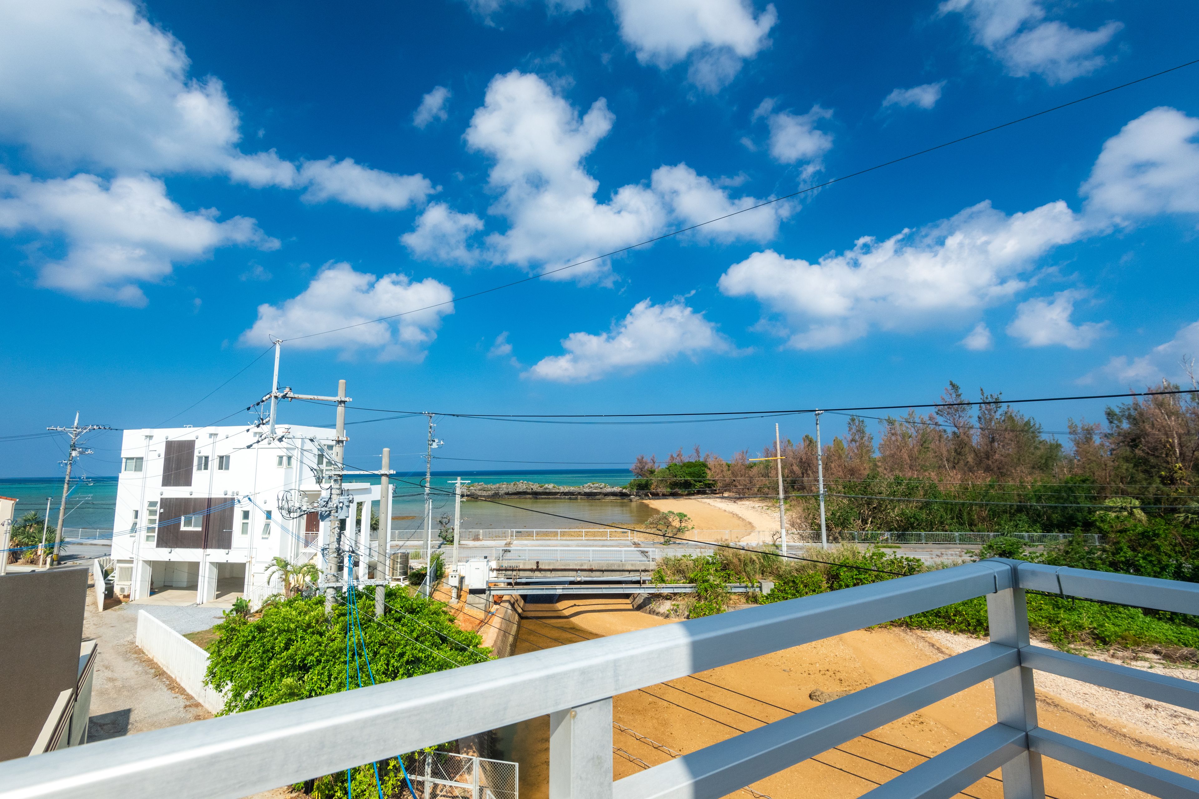 A coastal residential area with a clear view of the beach, a bridge, and a white building with multiple floors.