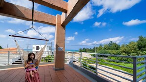 A balcony with a hammock, a view of the beach, and a railing. - Lanakai House (Onna)