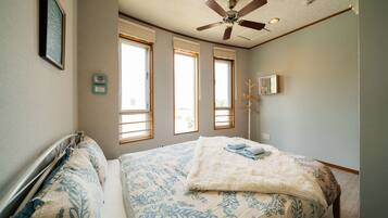 Um quarto com uma cama, um ventilador de teto e três janelas.