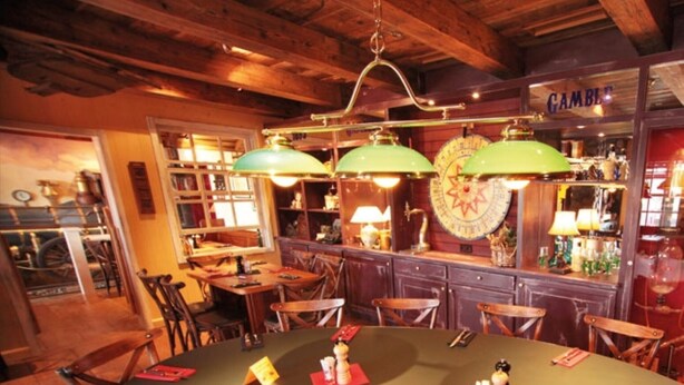 A cozy restaurant with a large round table set for dining, wooden chairs, and a bar area with a sign reading "GAMBLE". - Perfectly equipped apartment1 (Greifswald)