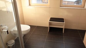 A small bathroom with a toilet, a sink, and a shower area. - Perfectly equipped apartment1 (Greifswald)