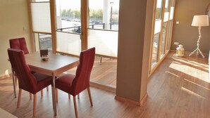 A modern hotel room with a dining area, a sofa, and a balcony with a view of the parking area. - Perfectly equipped apartment1 (Greifswald)