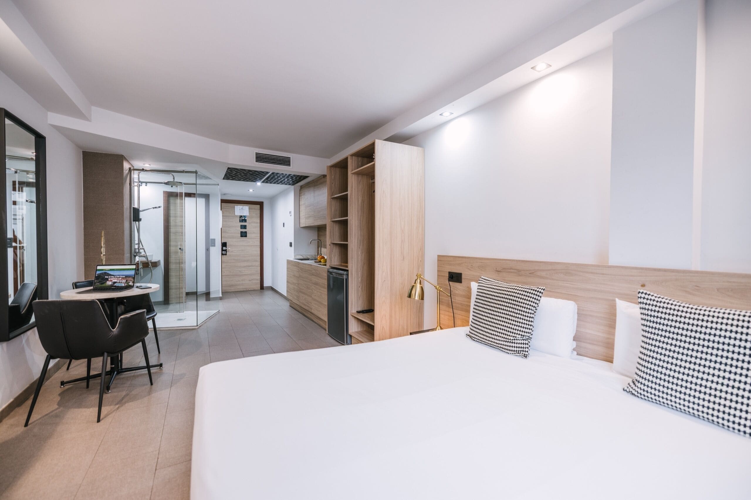 Una habitación de hotel moderna con una cama grande, un escritorio con una computadora portátil, una silla, un armario y un espejo.