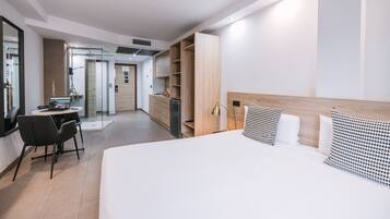 A modern hotel room with a large bed, a desk with a laptop, a chair, a wardrobe, and a mirror.