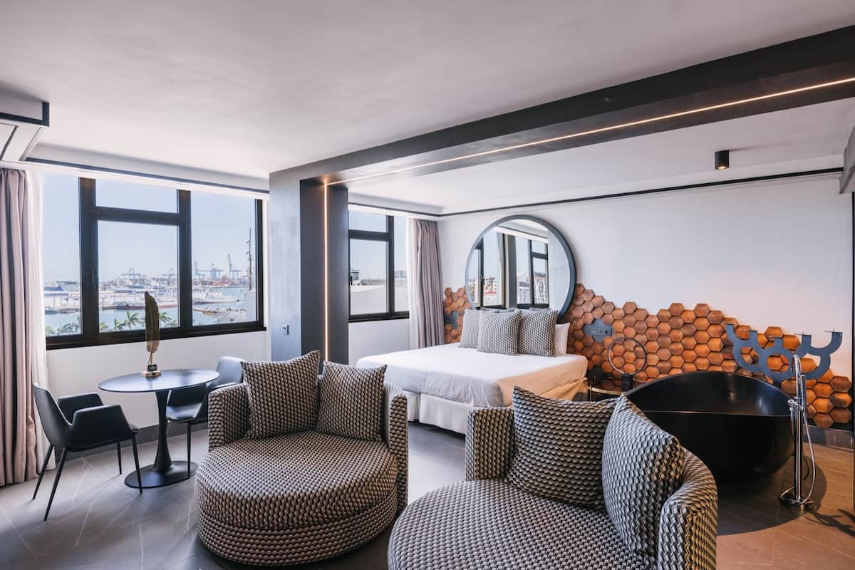 Ein modernes Hotelzimmer mit Bett, Sitzecke, großen Fenstern und einer besonderen Wandgestaltung.