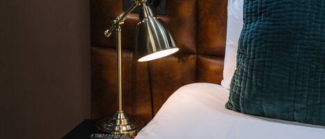 Una cama con cabecera, una lámpara de noche, un control remoto y una almohada color turquesa.