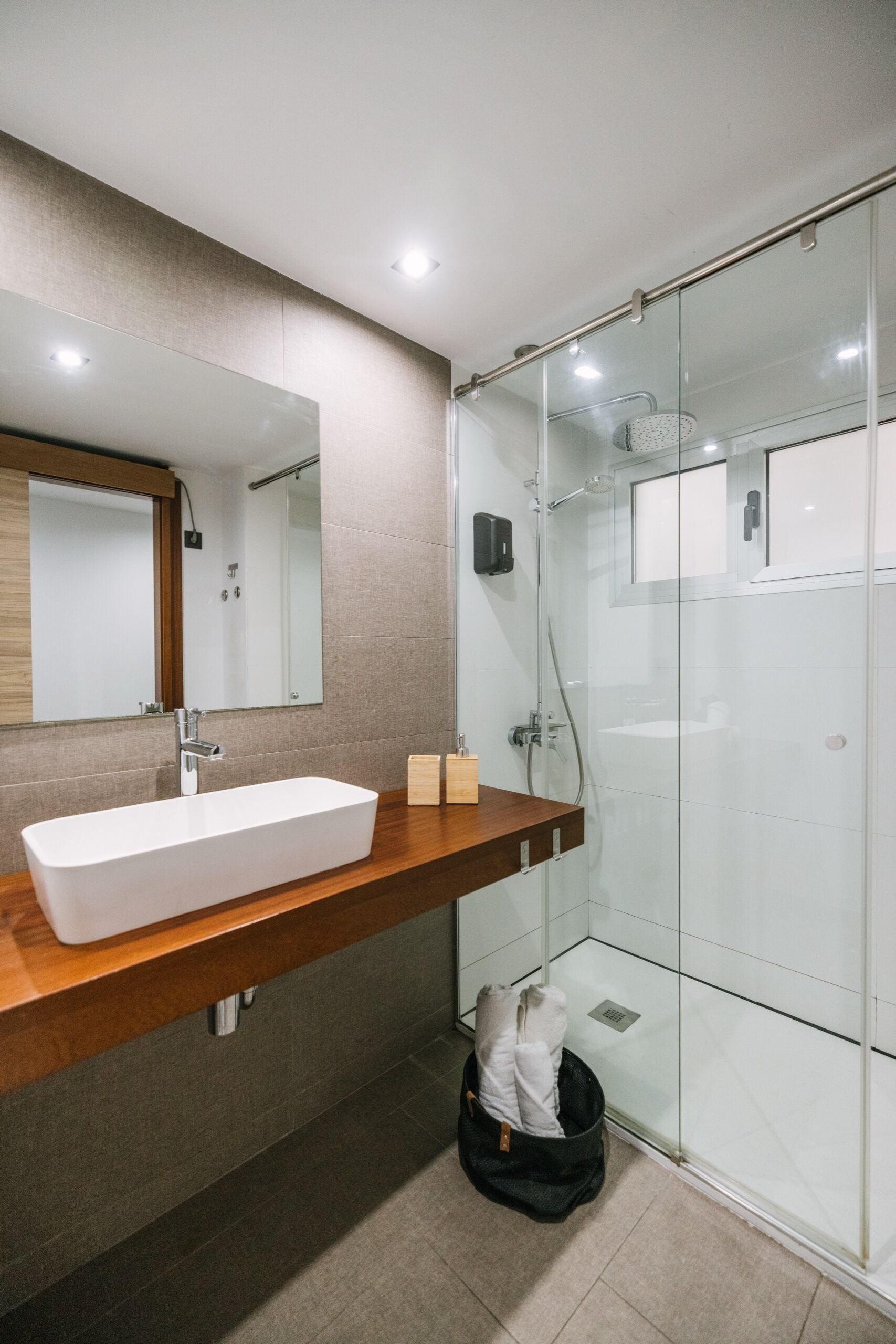 Een moderne badkamer met een rechthoekig wastafelmeubel, een douchecabine met glazen wanden en een houten opbergmeubel.