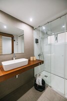 Ein modernes Badezimmer mit einem rechteckigen Waschbecken, einer Duschkabine aus Glas und einem Holz-Waschtisch.