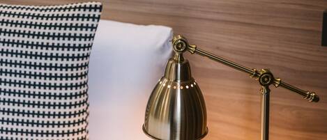 A bed with a white sheet, a black and white checkered pillow, and a brass desk lamp on a black nightstand.