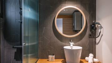 Un baño moderno con cabina de ducha de vidrio, tocador de madera, espejo redondo y un inodoro.