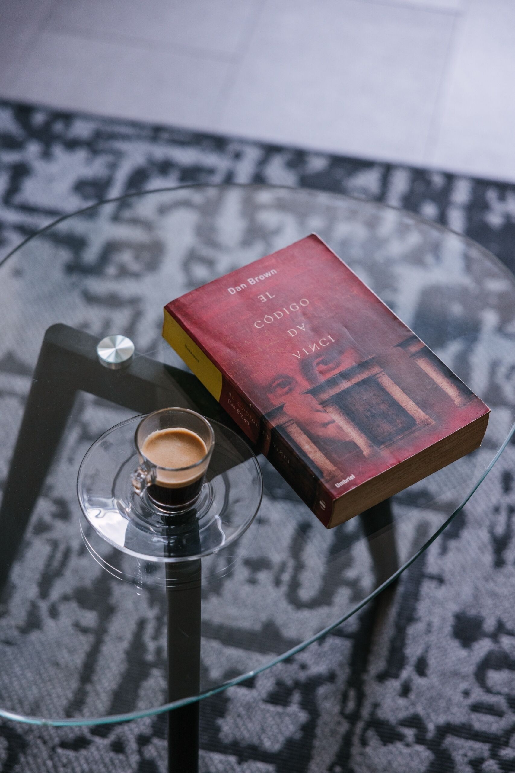 A book titled 'Codigo da Vinci' on a glass table with a coffee cup.