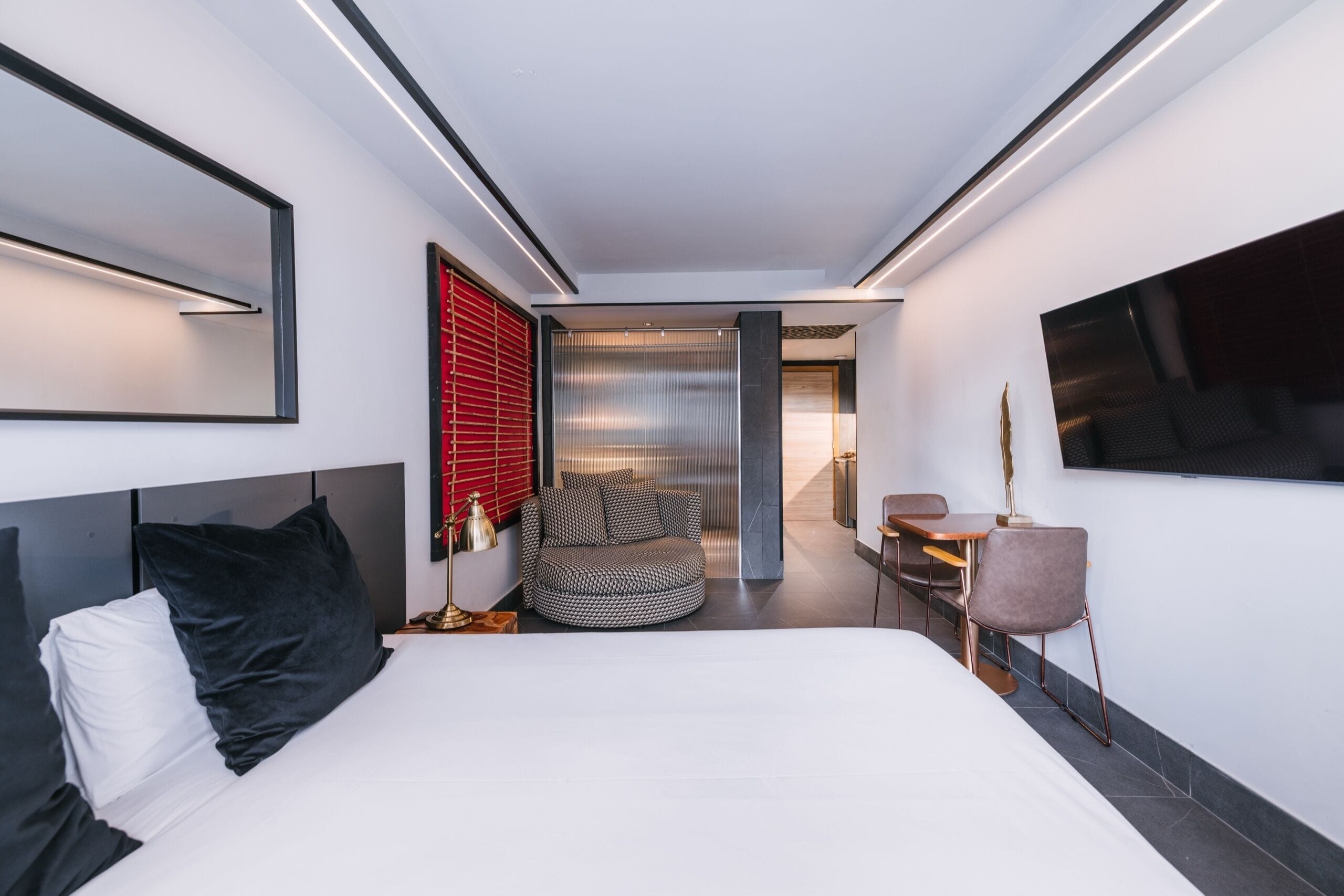Een moderne hotelkamer met een groot bed, een zithoek met een bank en stoelen, een bijzettafeltje en een flatscreen televisie aan de muur.