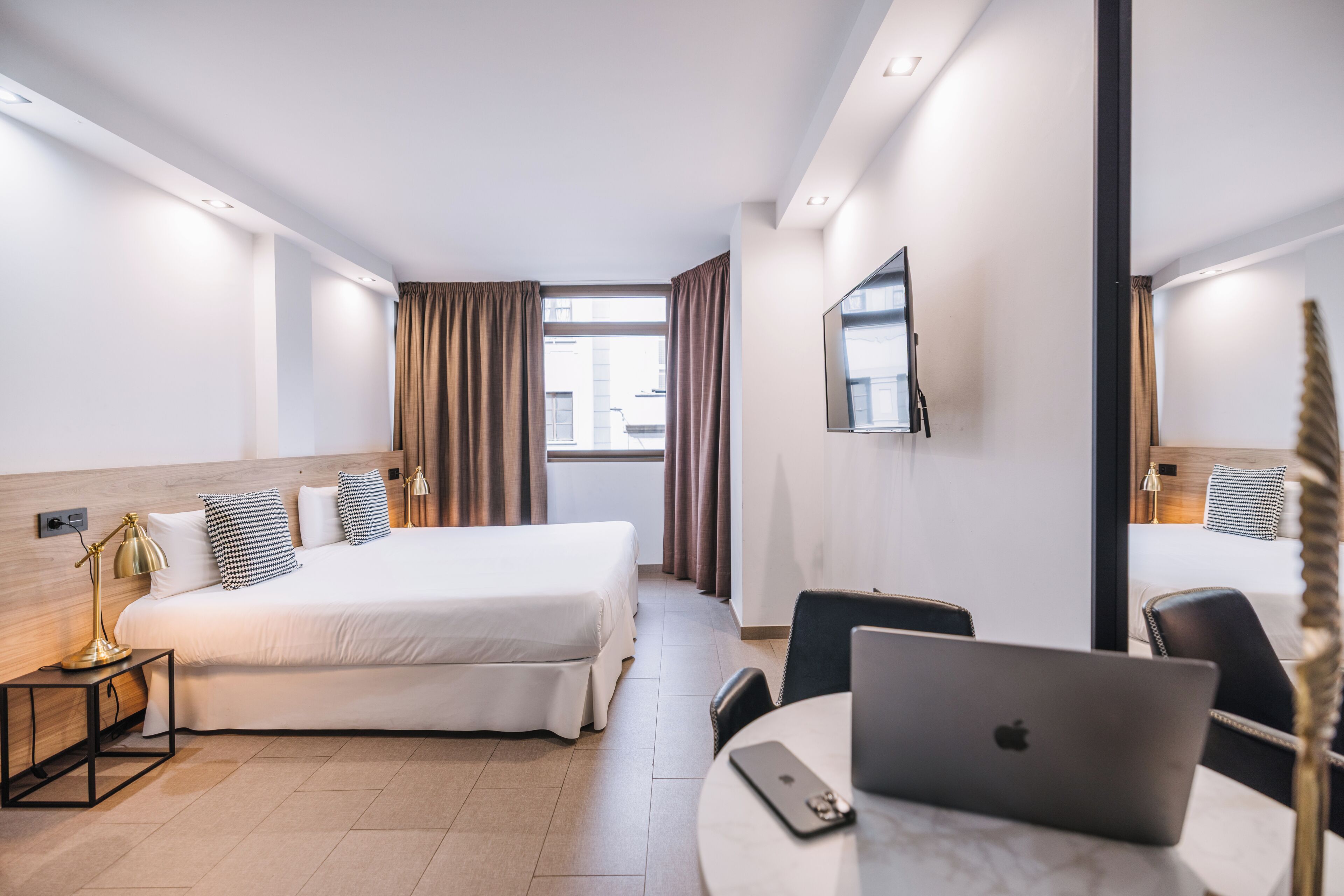 Une chambre d’hôtel avec un lit, un bureau avec un ordinateur portable, une chaise, une télévision et une fenêtre avec des rideaux.