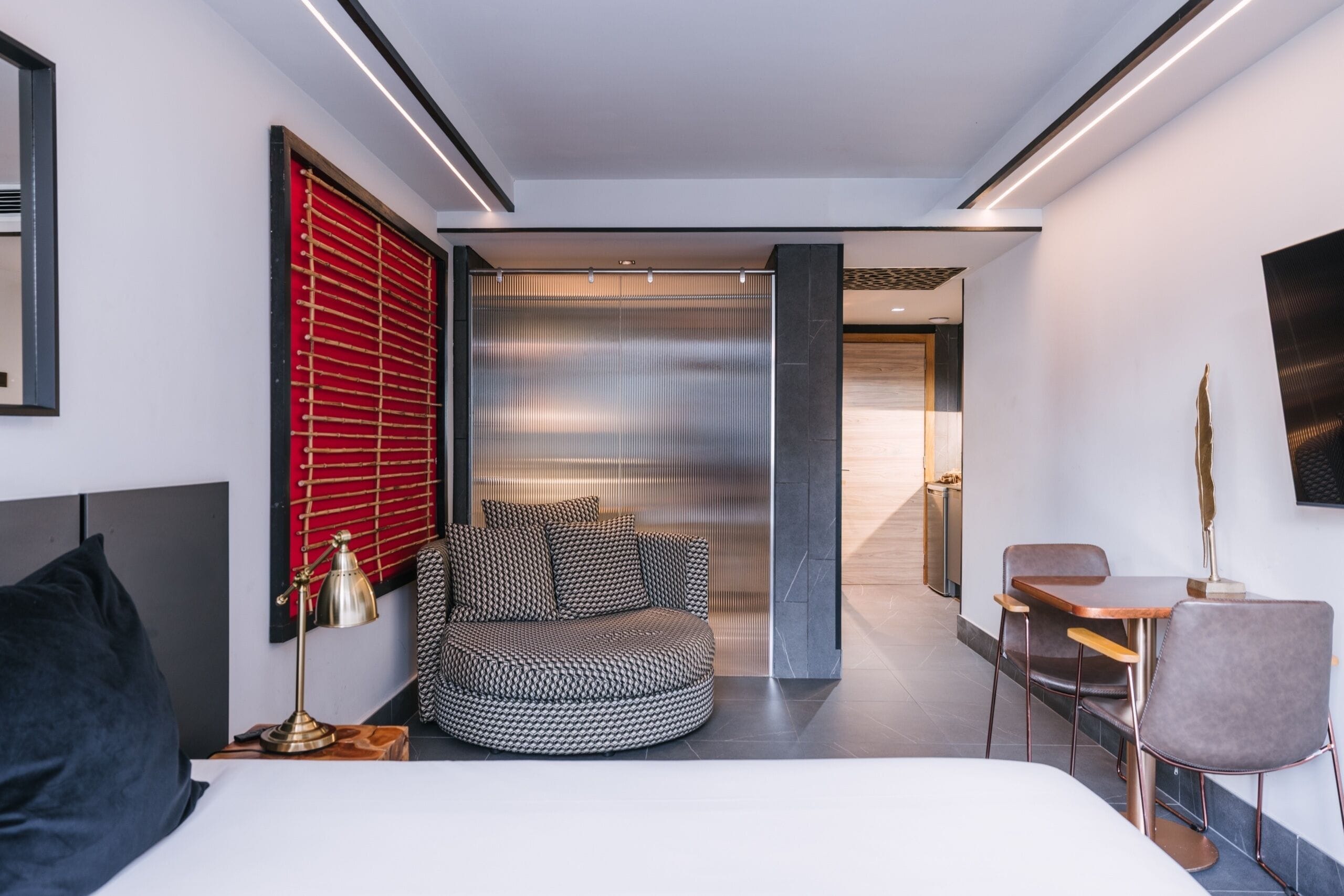 Una habitación de hotel moderna con una cama, una zona de estar circular, un escritorio y un televisor.