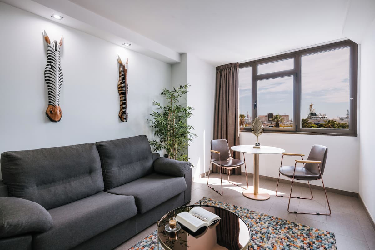 Ein modernes Wohnzimmer mit grauem Sofa, einem runden Couchtisch, einem kleinen runden Tisch mit zwei Stühlen, einem großen Fenster mit Blick und zwei an der Wand befestigten Tierbildhaupte.