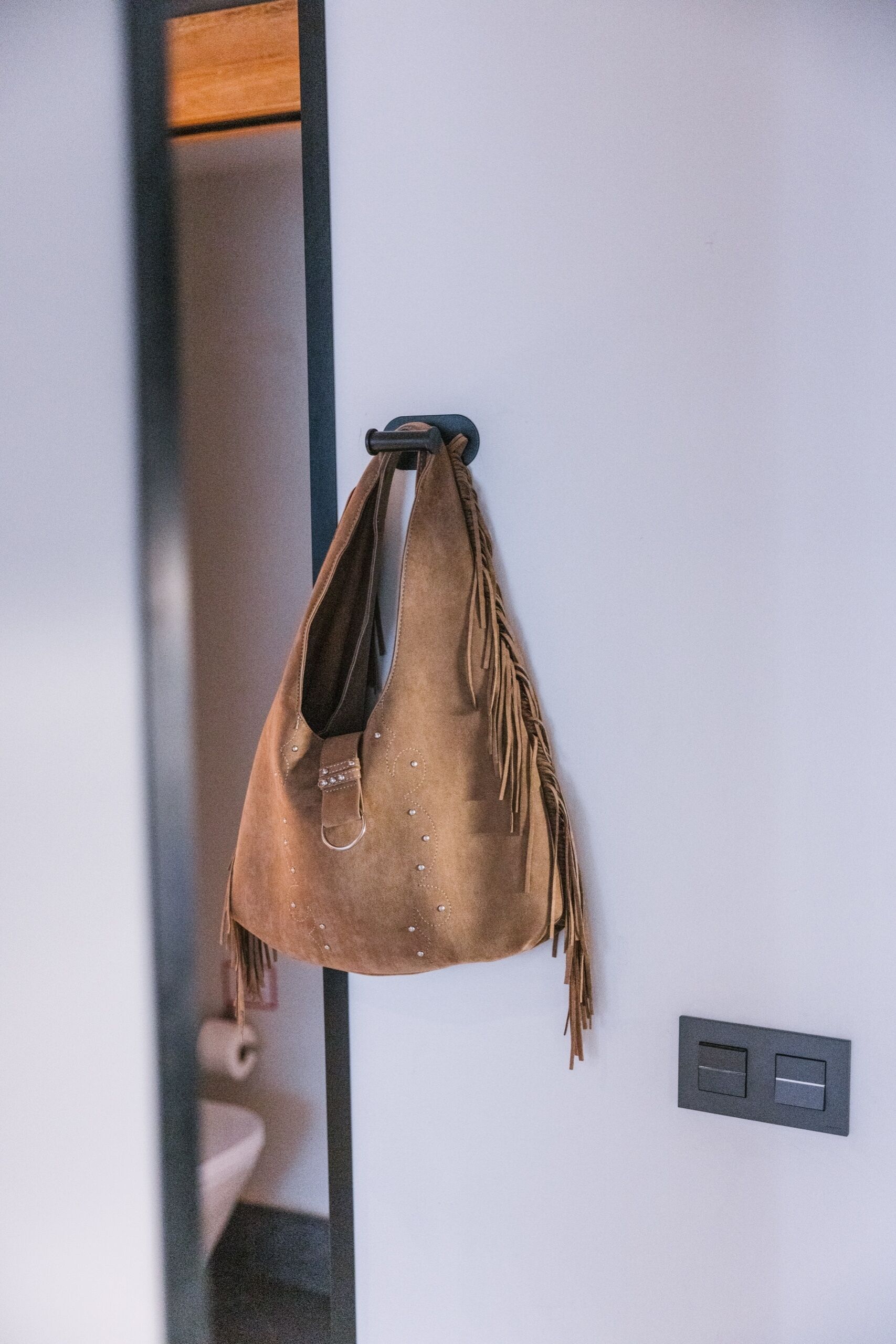 A brown bag hanging on a hook against a white wall with a switch nearby.