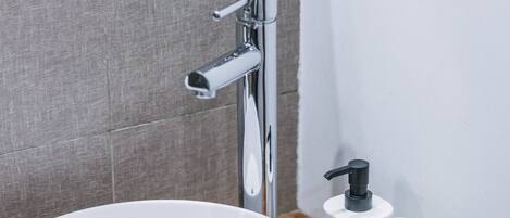 Un baño con lavamanos blanco, grifo cromado y espejo.