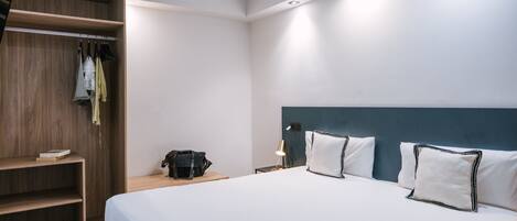 Habitación de hotel con cama, armario de madera, mesita de noche con lámpara y otra mesita junto a la cama.