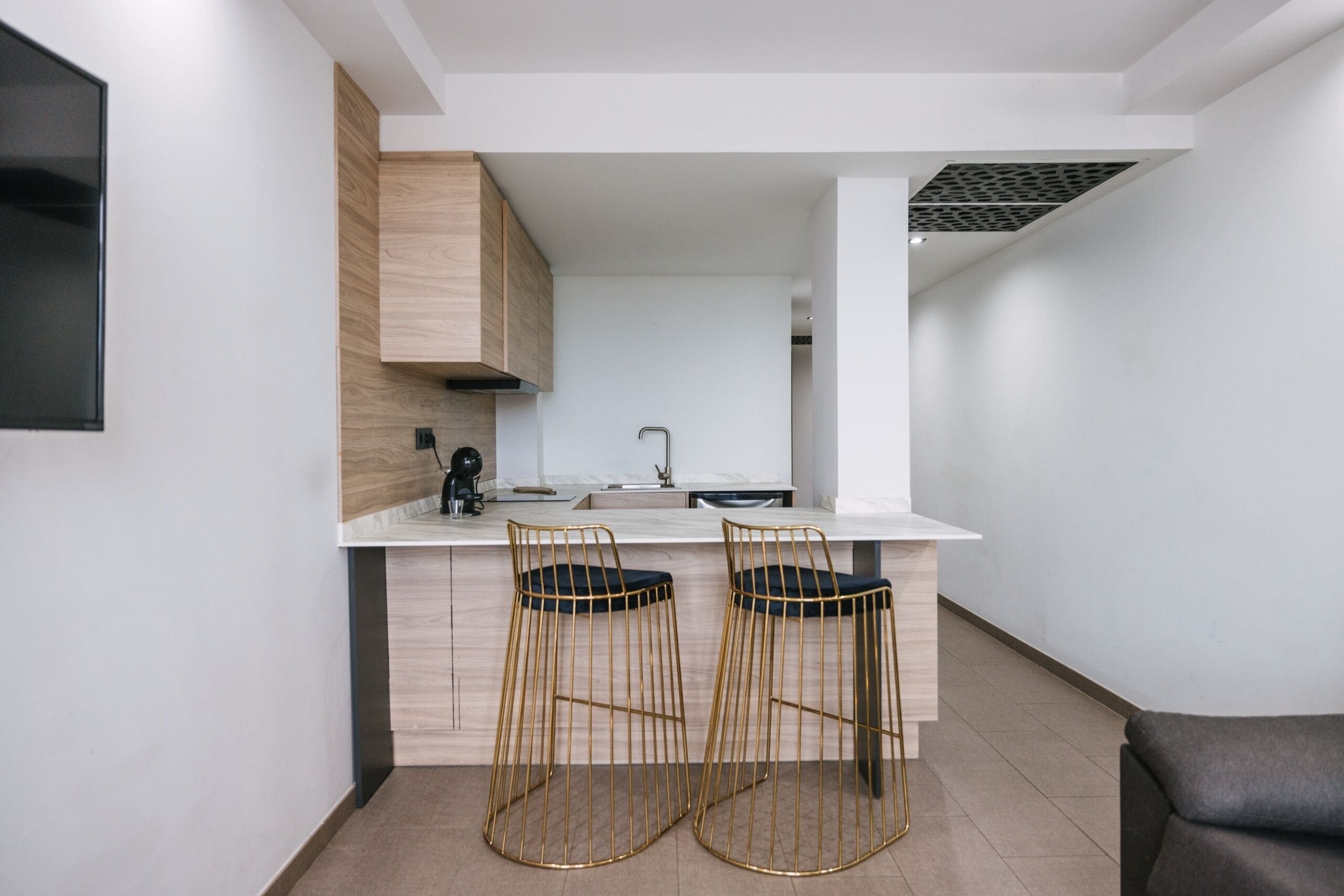 A modern kitchen with two bar stools, a white countertop, and a built-in oven.