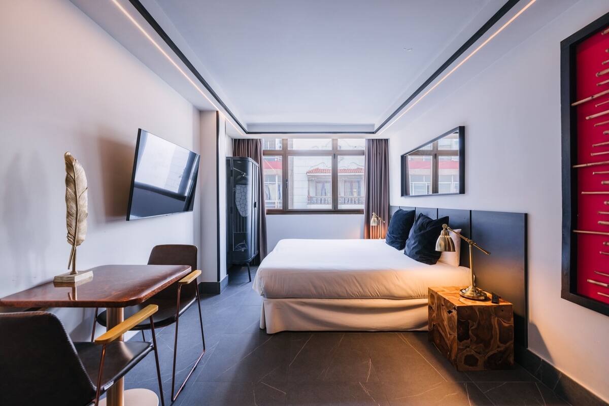 Ein modernes Hotelzimmer mit Bett, Schreibtisch, Stuhl, Fernseher und Blick ins Freie.