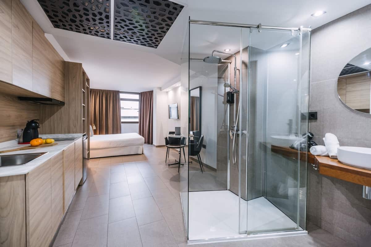 Ein modernes Hotelzimmer mit Küchenzeile, einer in Glas gefassten Dusche, einer Sitzecke und einem Essbereich.