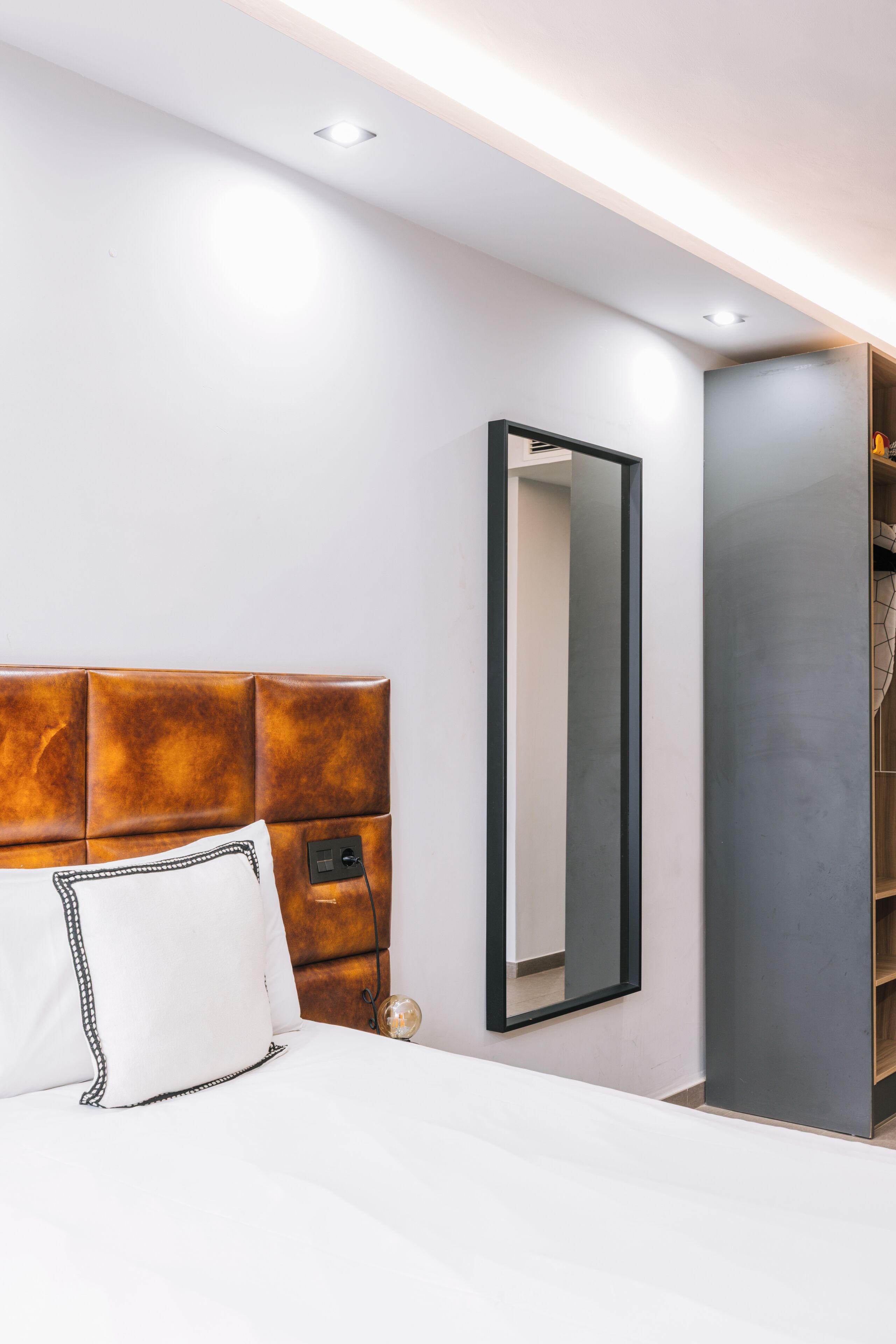 A modern hotel room with a bed, a large mirror, and a built-in wardrobe.