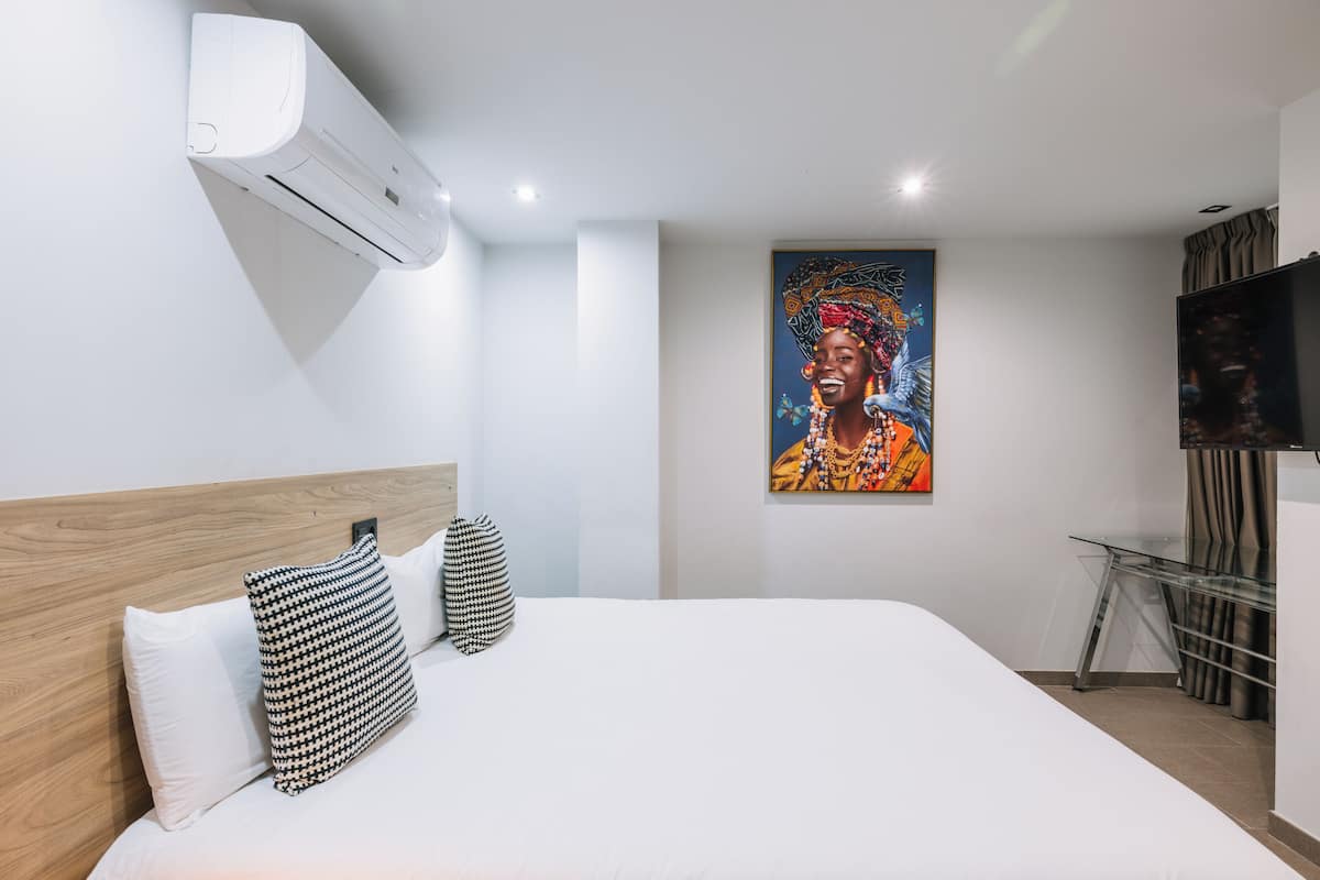 Ein modernes Hotelzimmer mit einem großen Bett, einer Klimaanlage, einem Gemälde, einem Fernseher und einem Schreibtisch mit Stuhl.