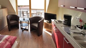 A compact room with a bed, two chairs, a small table, a kitchenette, and a balcony with a view. - With much love furnished oasis of well-being. (Greifswald)