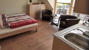 A compact room with a bed, a small kitchenette, a chair, and a view of the outdoors. - With much love furnished oasis of well-being. (Greifswald)