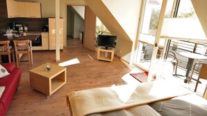 A modern living room with a red sofa, wooden coffee table, and a dining area with a kitchen in the background. - Modern furnished apartment for the family (Greifswald)