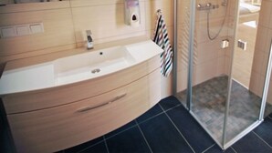A modern bathroom with a sink, mirror, and shower. - Modern furnished apartment for the family (Greifswald)