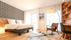 Una habitación de hotel moderna con una cama, una silla, un escritorio, un ventanal grande y una pared con diseño.