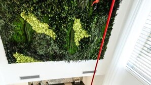 Una cocina moderna con una pared verde integrada, un comedor con una mesa redonda y sillas, y una lámpara colgante roja.