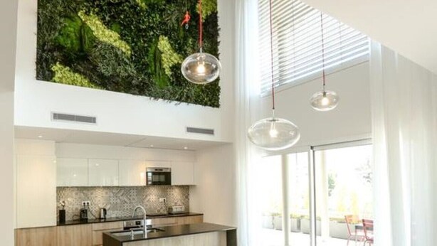 Una cocina moderna con una isla central, armarios blancos y un jardín vertical verde.