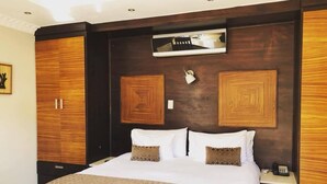 Une chambre d’hôtel avec un grand lit, une tête de lit en bois, deux armoires, une table de chevet avec une lampe et un petit tiroir de chevet.