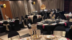 Une salle de banquet avec des tables rondes dressées pour un événement formel, agrémentée d’assiettes à bordure dorée et d’une pièce décorative centrale.