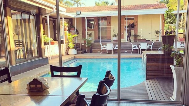 Un espace piscine extérieur moderne, doté d’une table et de chaises, et entouré de portes et de fenêtres en verre.