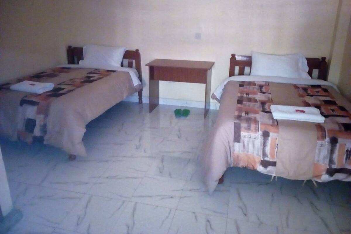 A room with two beds, a small table, and a pair of slippers on the floor.