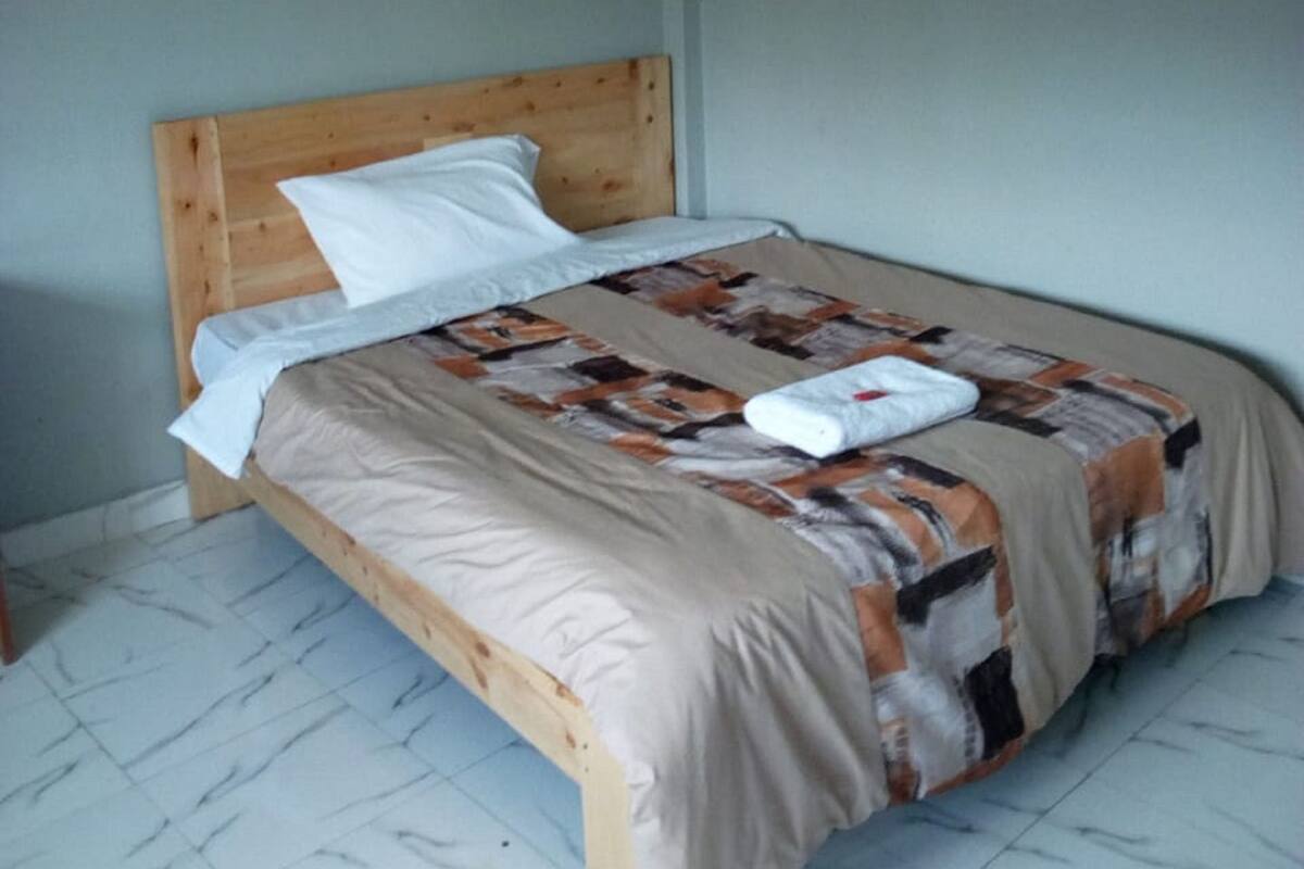 A single bed with a wooden headboard, a patterned bedspread, and a white pillow.