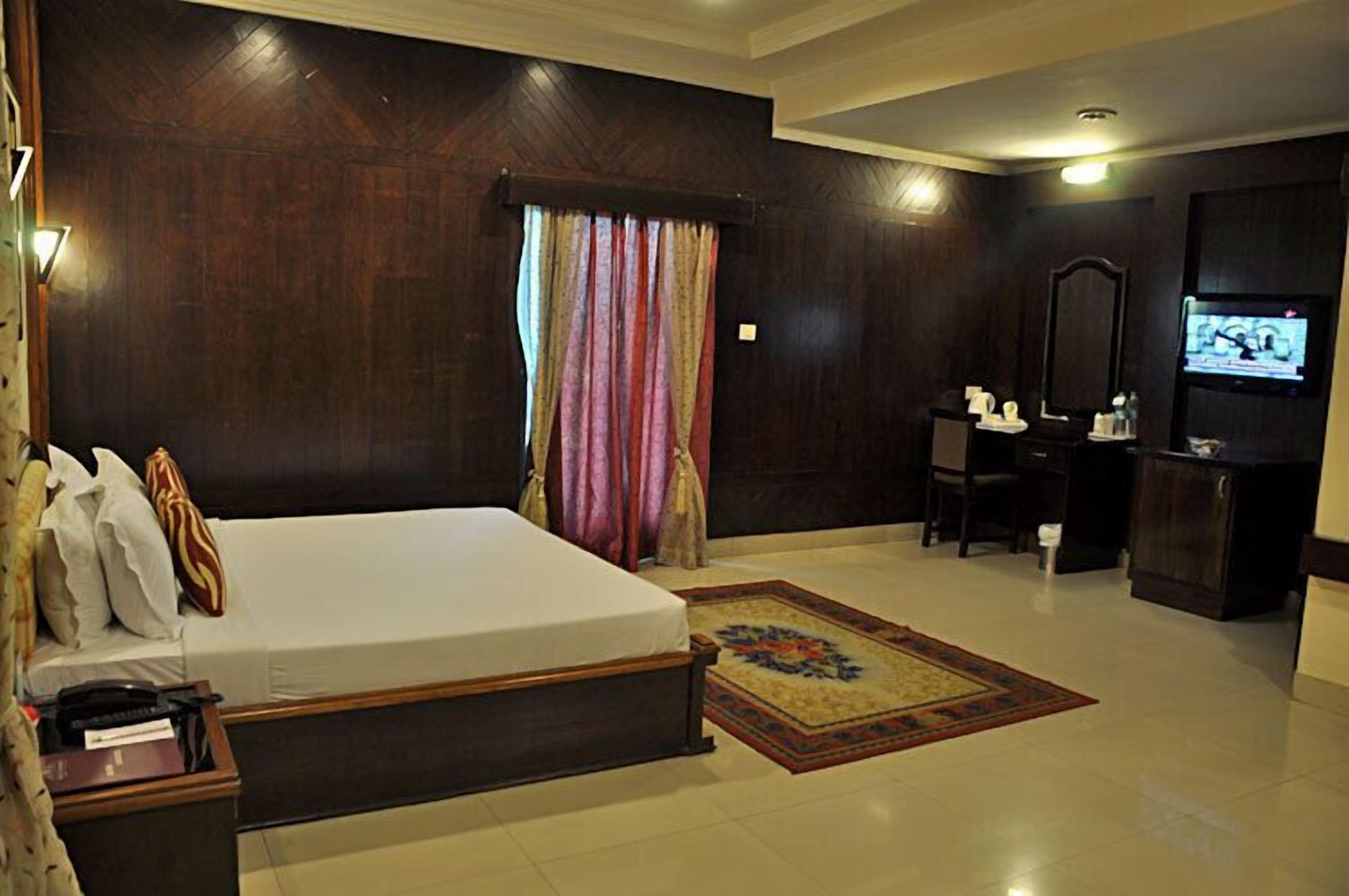 A hotel room with a large bed, a desk with a chair, a television, and a mirror.
