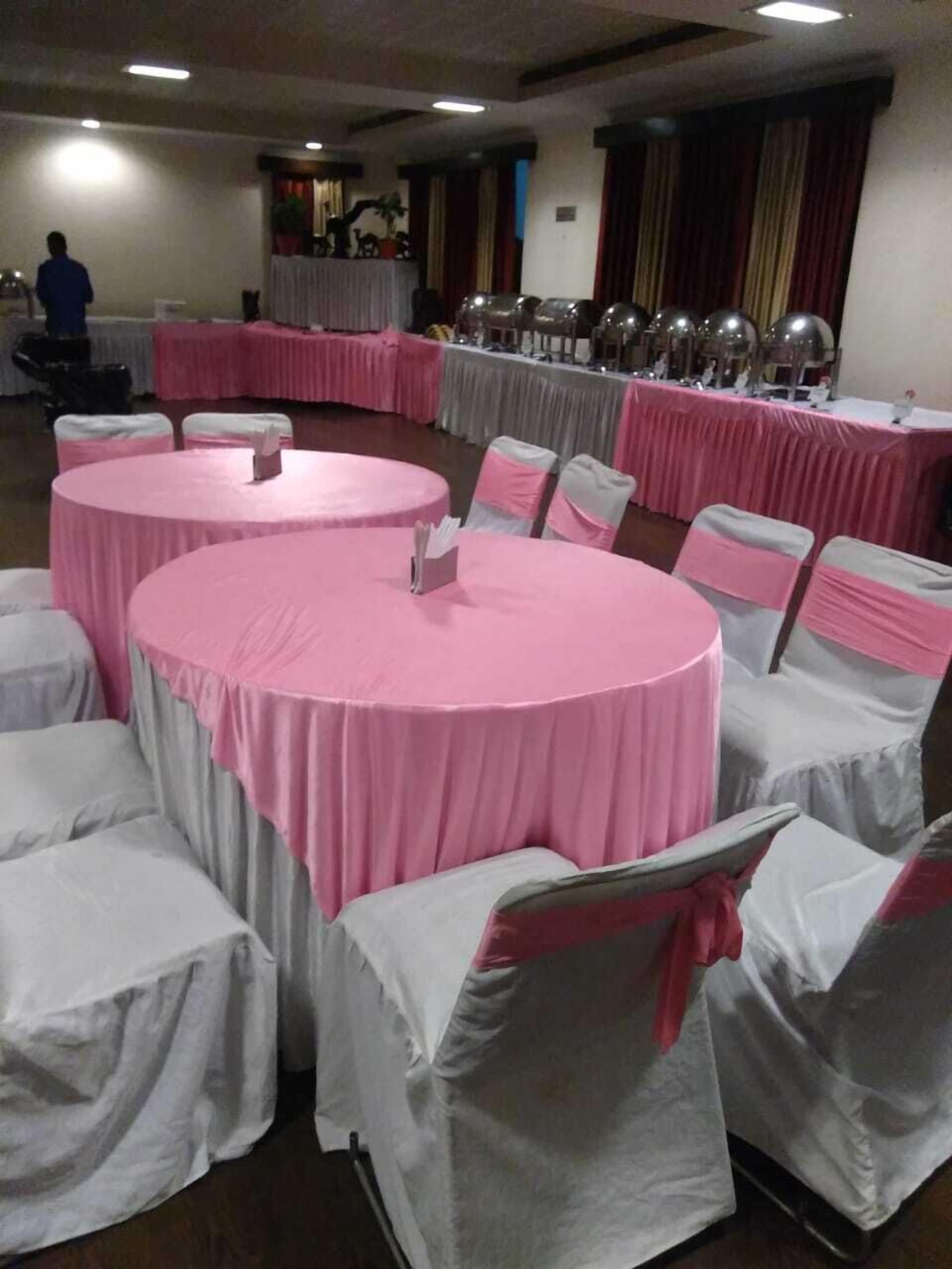 A banquet hall with round tables covered in pink tablecloths, white chairs with pink sashes, and a long table with a white tablecloth in the background.