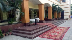 A hotel entrance with a red carpet, steps leading to a covered area, and potted plants. - Hotel Rudra Continental Rudrapur (Kichha)