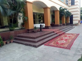 A hotel entrance with a red carpet, steps leading to a covered area, and potted plants.