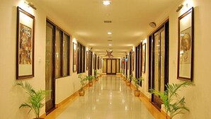 A long, well-lit hallway with framed artwork on the walls, potted plants along the sides, and a shiny floor. - Hotel Rudra Continental Rudrapur (Kichha)