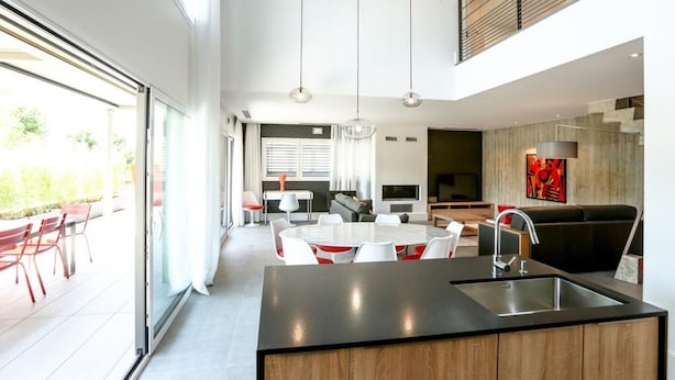 Uma cozinha moderna com ilha central, sala de jantar com mesa redonda e área de estar com sofá e televisão.