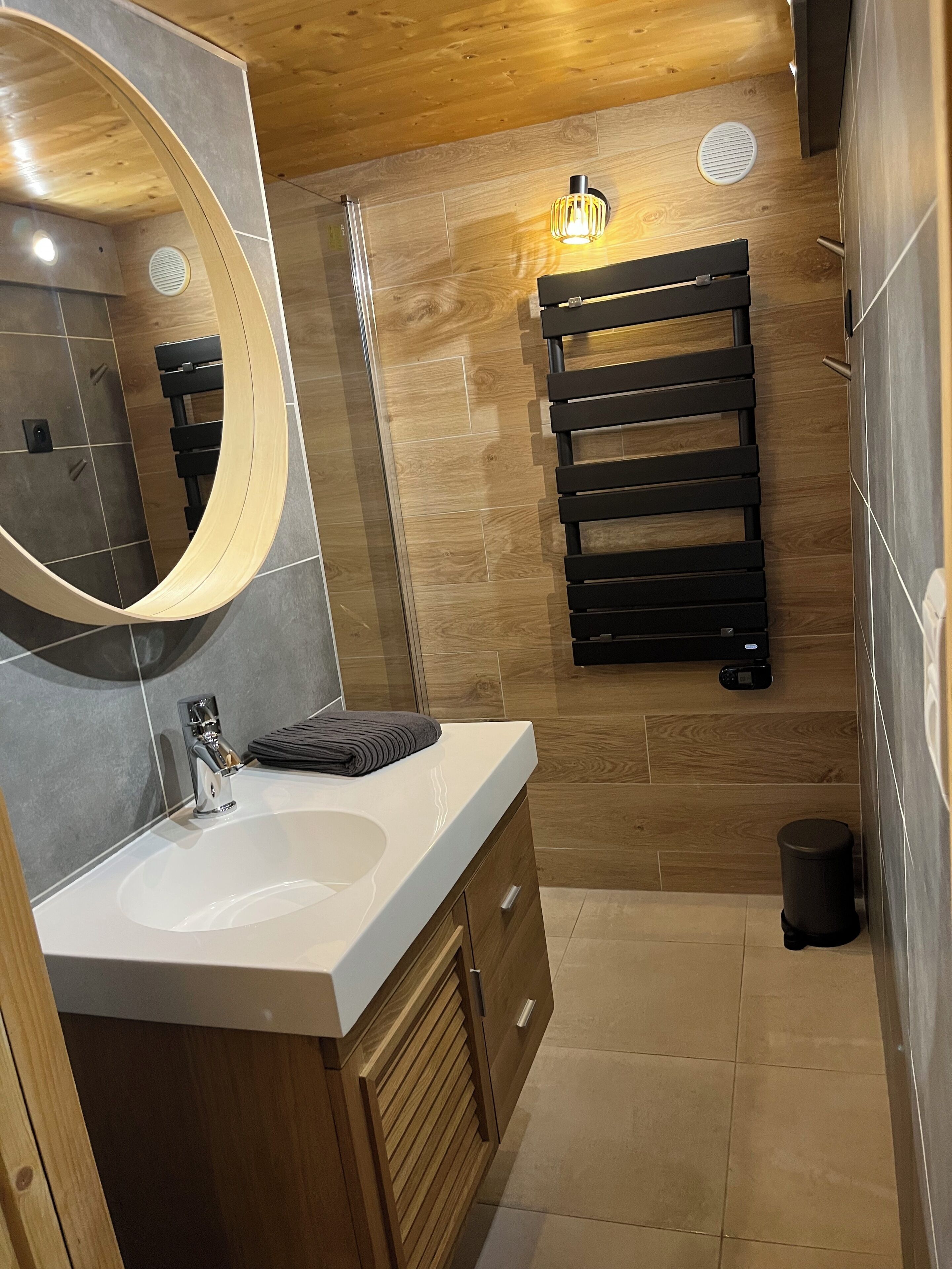 A modern bathroom with a wooden vanity, a large mirror, a towel rack, and a shower area.