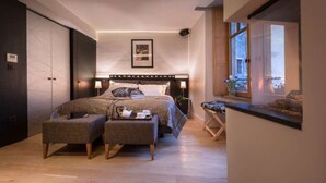 A modern bedroom with a large bed, a bedside table, a small seating area, and a window with a view. - Lodges - Studio + Duplex (Annecy)
