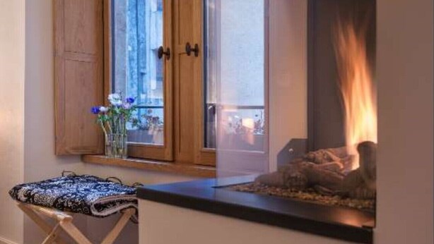 A cozy room with a fireplace, wooden cabinets, and a window overlooking a cityscape. - Lodges - Studio + Duplex (Annecy)