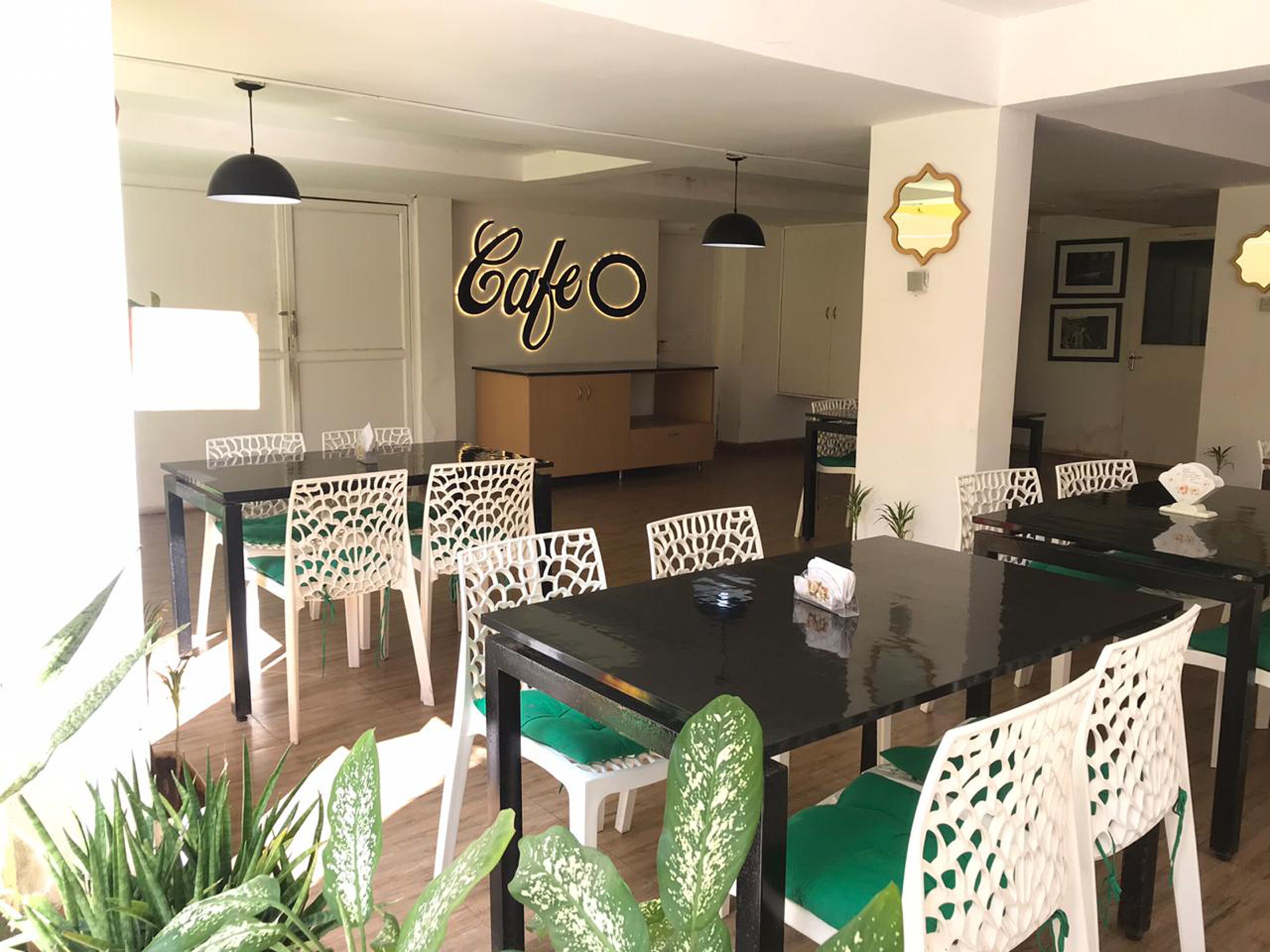 A dining area with a black table and white chairs, a kitchen in the background, and a sign that reads "Cafe".